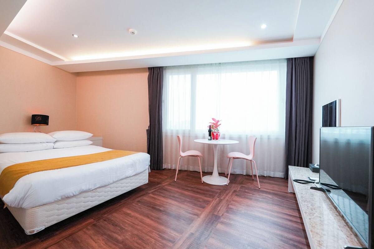 Une chambre d’hôtel équipée d’un lit, d’un bureau, d’une chaise, d’une télévision et d’une fenêtre avec des rideaux.