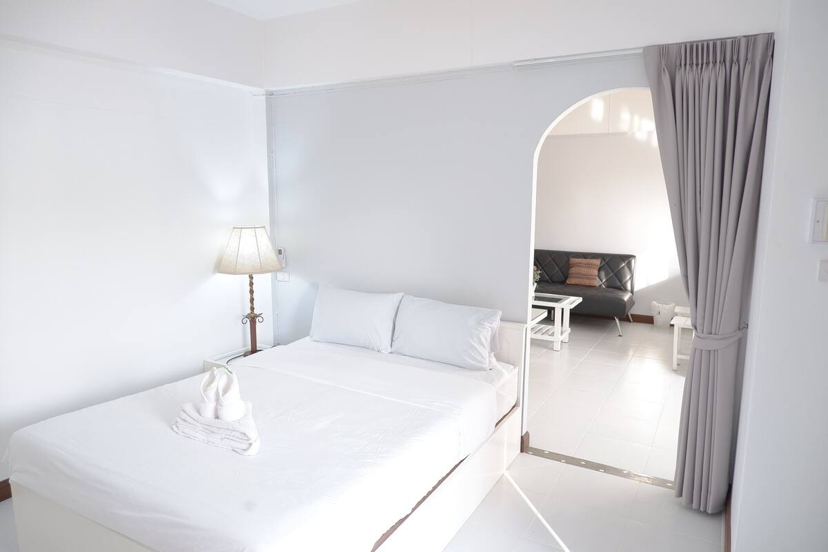 Een moderne hotelkamer met een bed, nachtkastje, lamp en uitzicht op een zithoek door een boog.