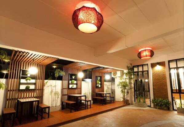 An outdoor seating area with wooden tables and chairs, surrounded by vertical wooden slats and potted plants.