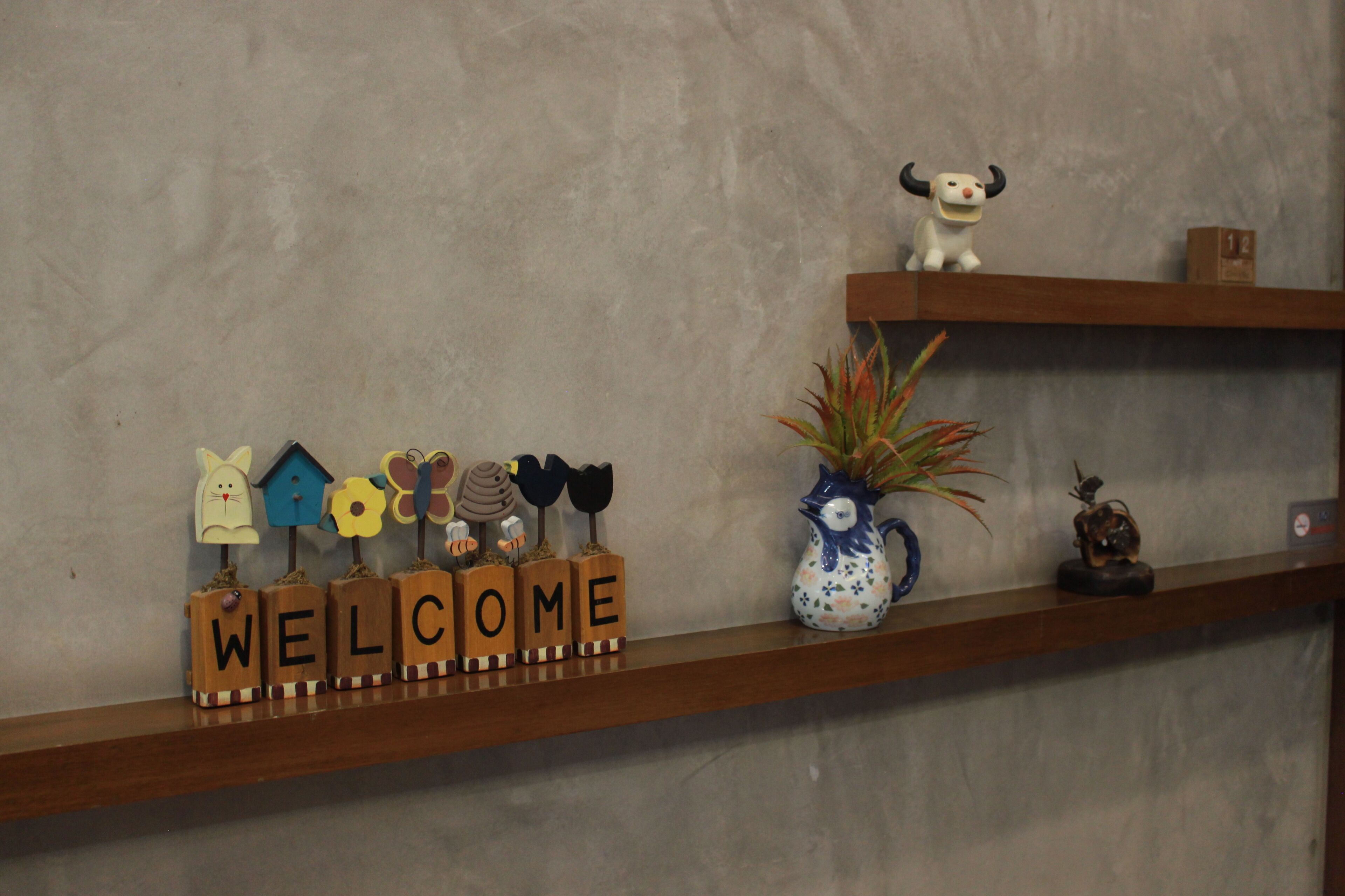 A shelf with wooden blocks spelling "WELCOME," a ceramic pitcher, and a small figurine.