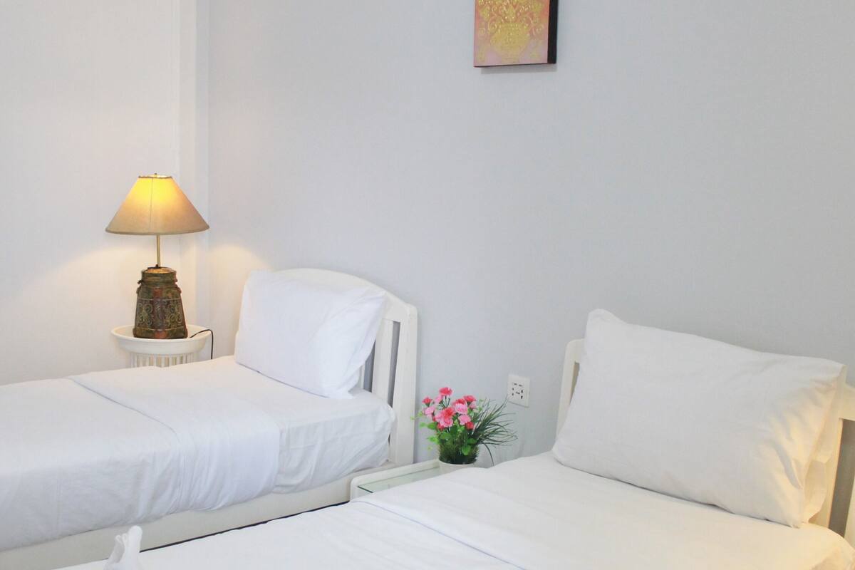 Een hotelkamer met twee enkele bedden, een nachtkastje met een lamp en een kleine potplant op de nachtkast.