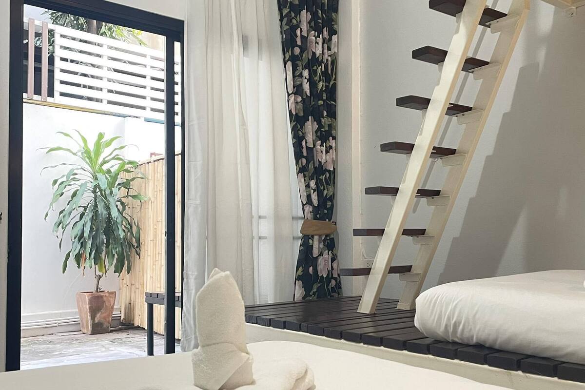 Een slaapkamer met een bed, een houten trap, een plant in pot en uitzicht op buiten.