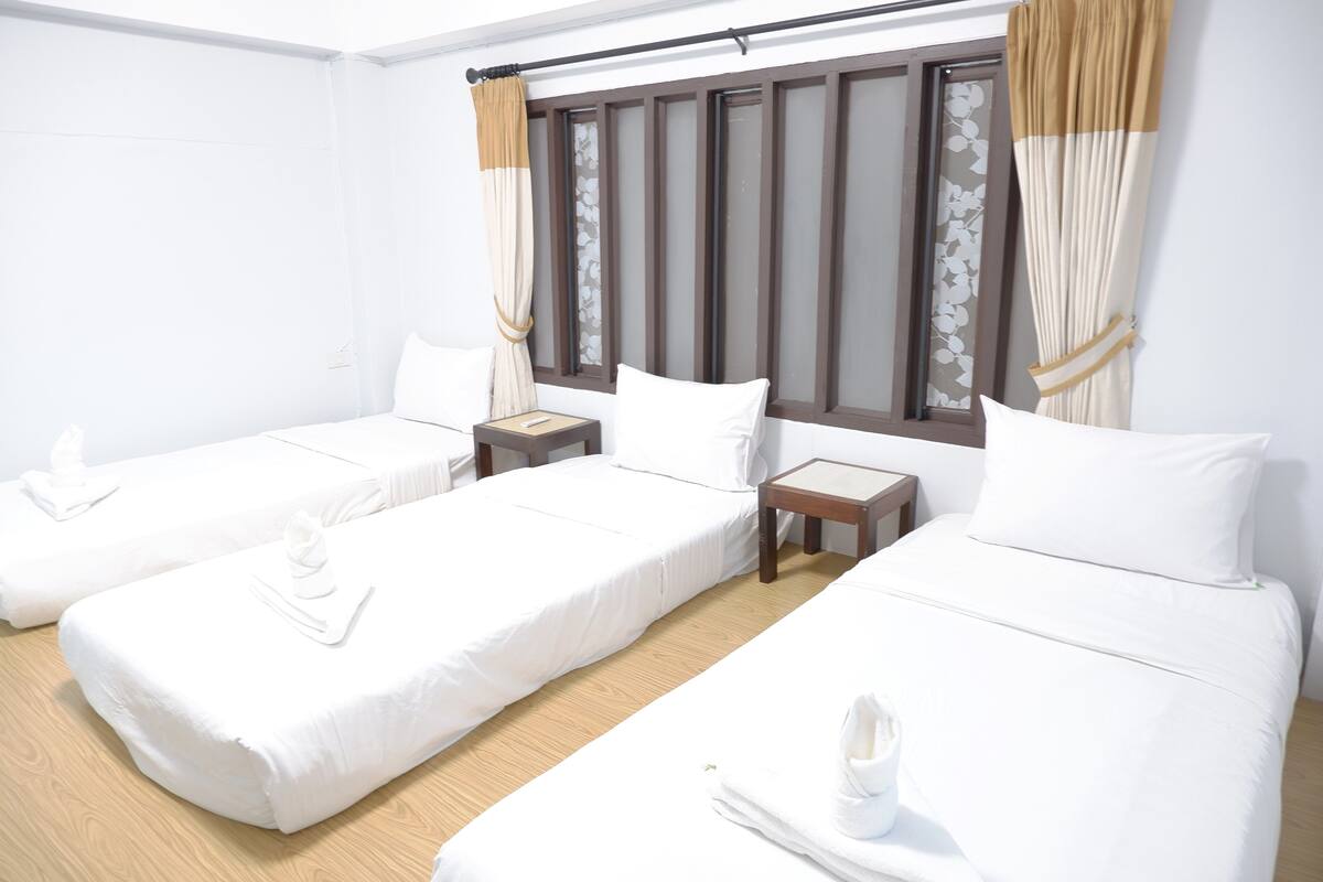Een hotelkamer met twee eenpersoonsbedden, een tafeltje en een raam met gordijnen.