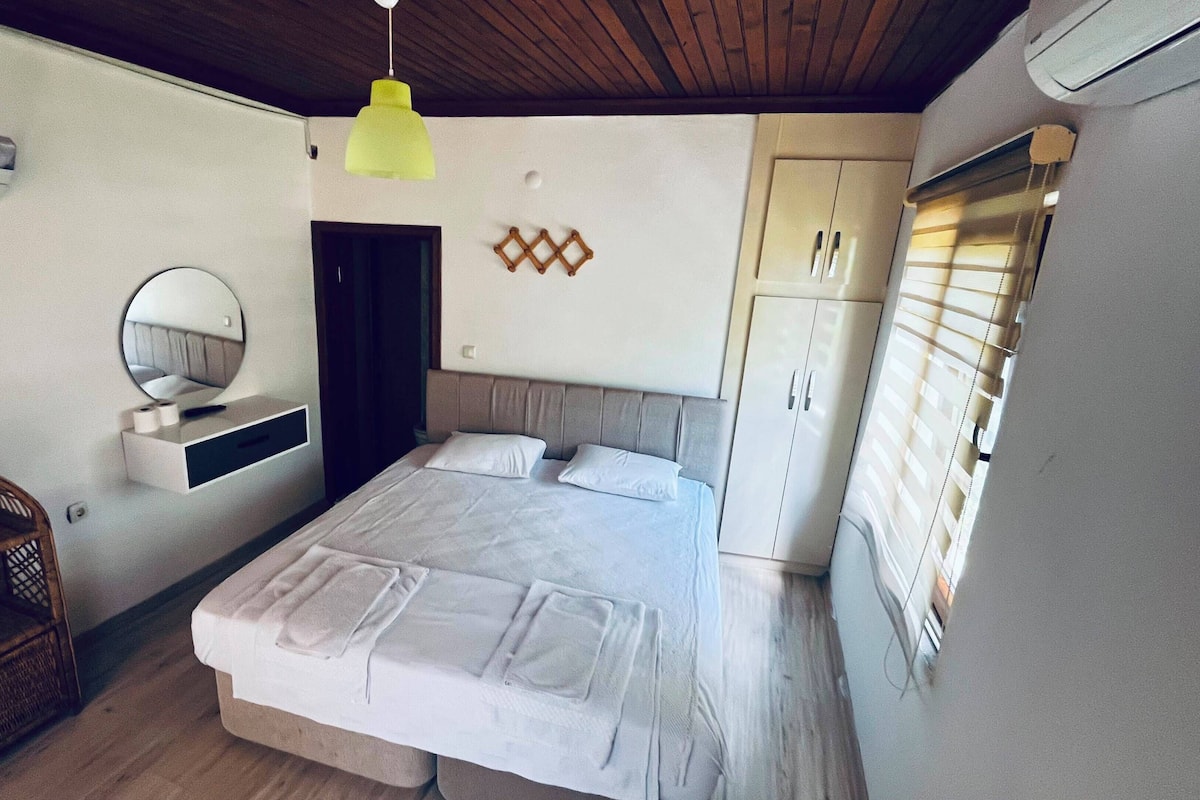 A bedroom with a bed, bedside table, mirror, wardrobe, and a hanging light fixture.