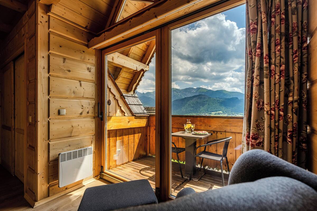 A wooden cabin with a balcony, a table, and chairs.