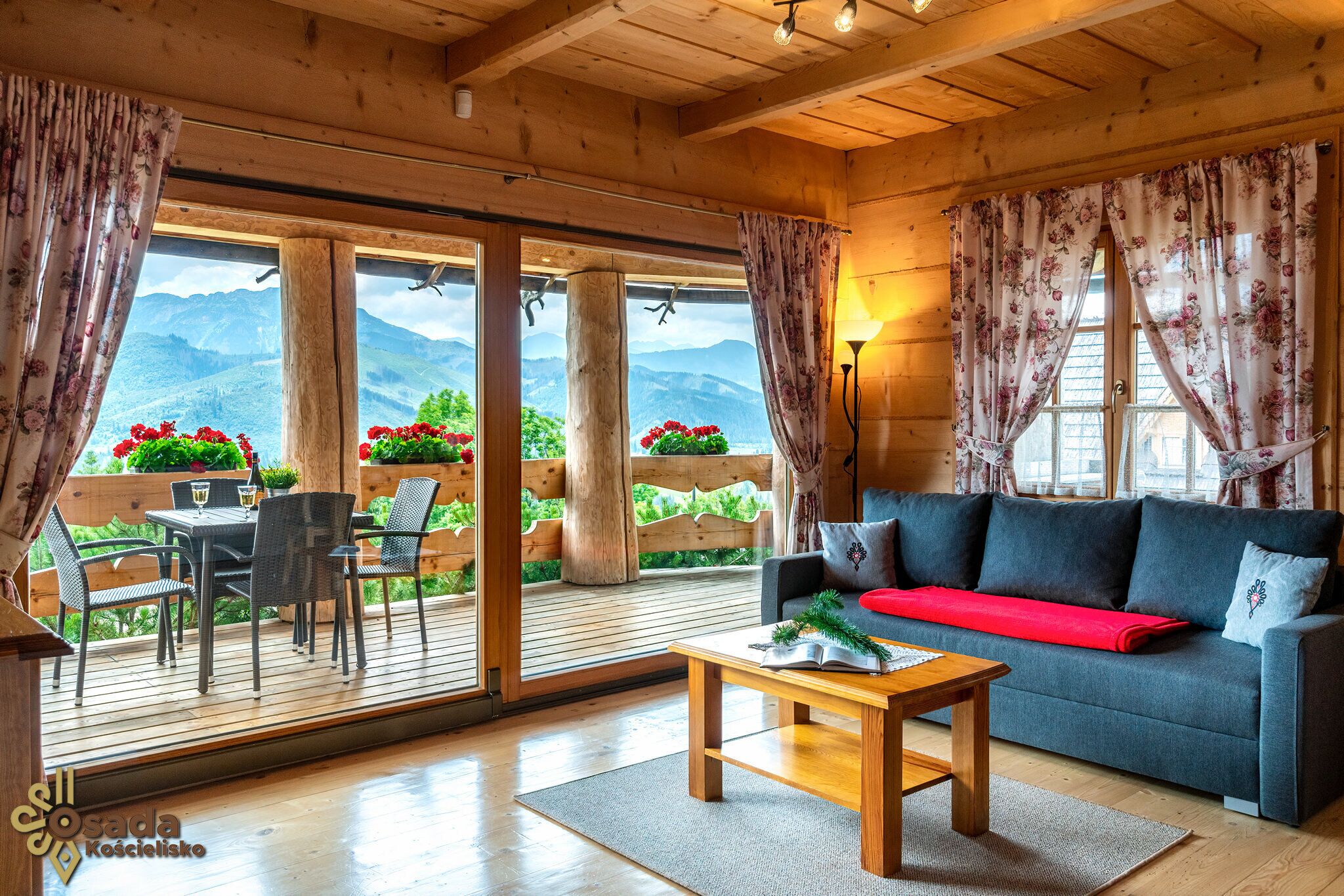 Une pièce chaleureuse avec un plafond en bois, un canapé, une table basse et une vue sur les montagnes grâce à de grandes fenêtres.