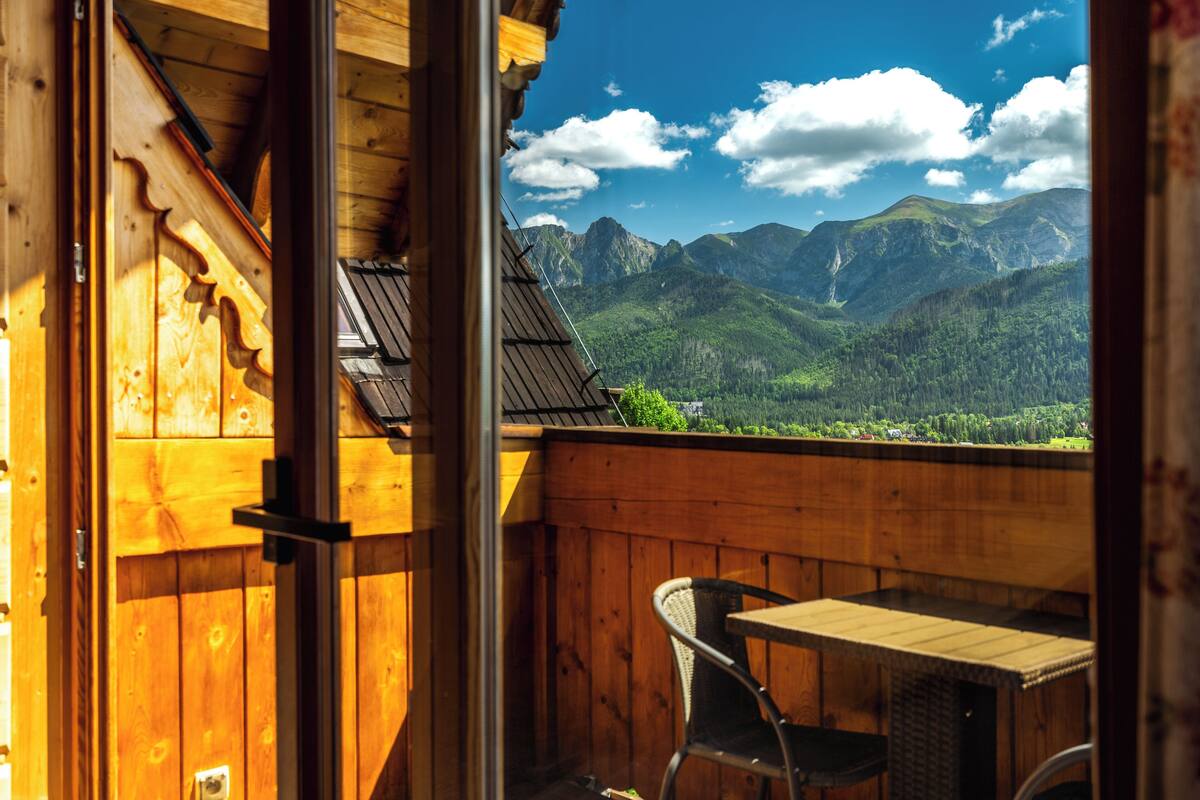 A wooden balcony with a table and chair, overlooking a mountainous landscape.