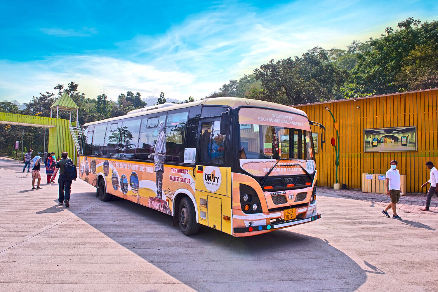 A bus with advertisements for a statue tour, parked at a bus station with people around.