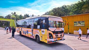 A bus with advertisements for a statue tour, parked at a bus station with people around.