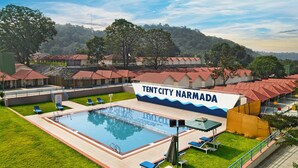 Zona de piscina con un letrero que dice "Tentcity Narmada", rodeada de sillas de descanso y un césped.