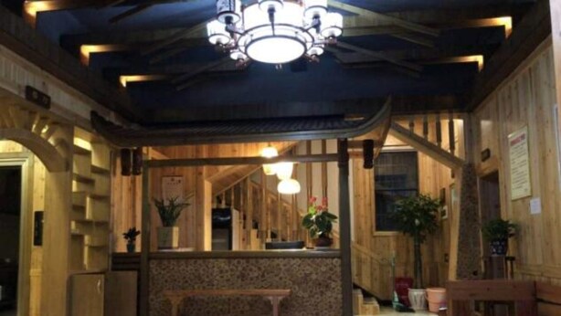 A wooden interior with a central bench, a chandelier, and potted plants.