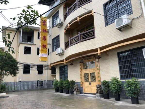 A building with a traditional architectural style, featuring a prominent wooden door with decorative metalwork, multiple windows with bars, and a yellow sign with red characters.