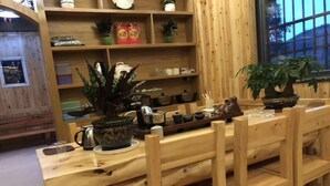 A wooden dining area with a long table and chairs, shelves with various items, and potted plants.