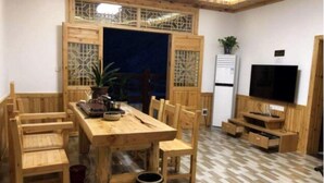 A compact living space with a wooden dining table and chairs, a small kitchen area with a refrigerator and a TV, and a patterned floor.