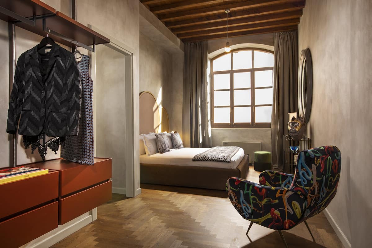 Une chambre à coucher avec un lit, une commode, une chaise et une fenêtre avec des rideaux.