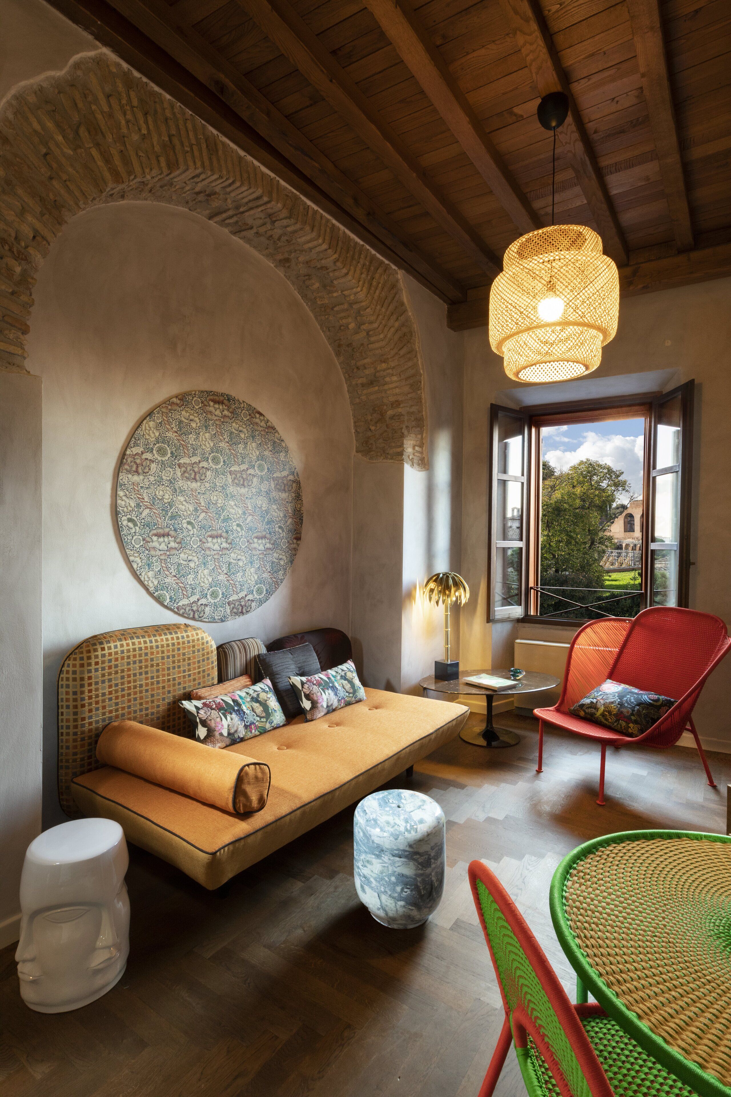 A cozy room with a wooden ceiling, a round wall hanging, a sofa with cushions, a red chair, and a round table.