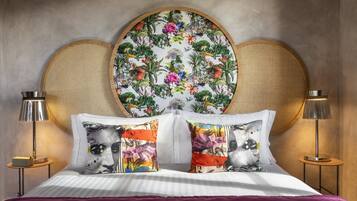 Una cama con cabecera estampada con motivos florales, dos lámparas de noche y una manta morada.