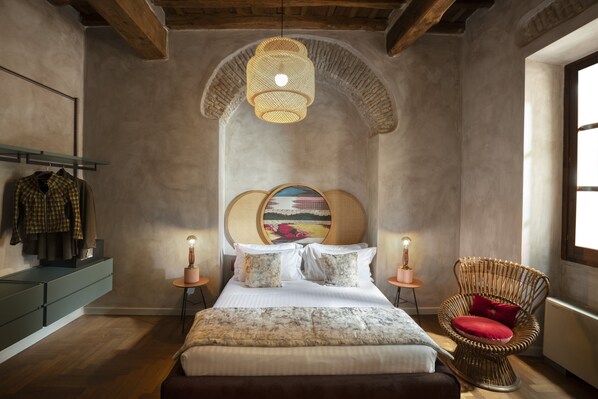 Une chambre avec un grand lit, une chaise en osier et un luminaire suspendu.