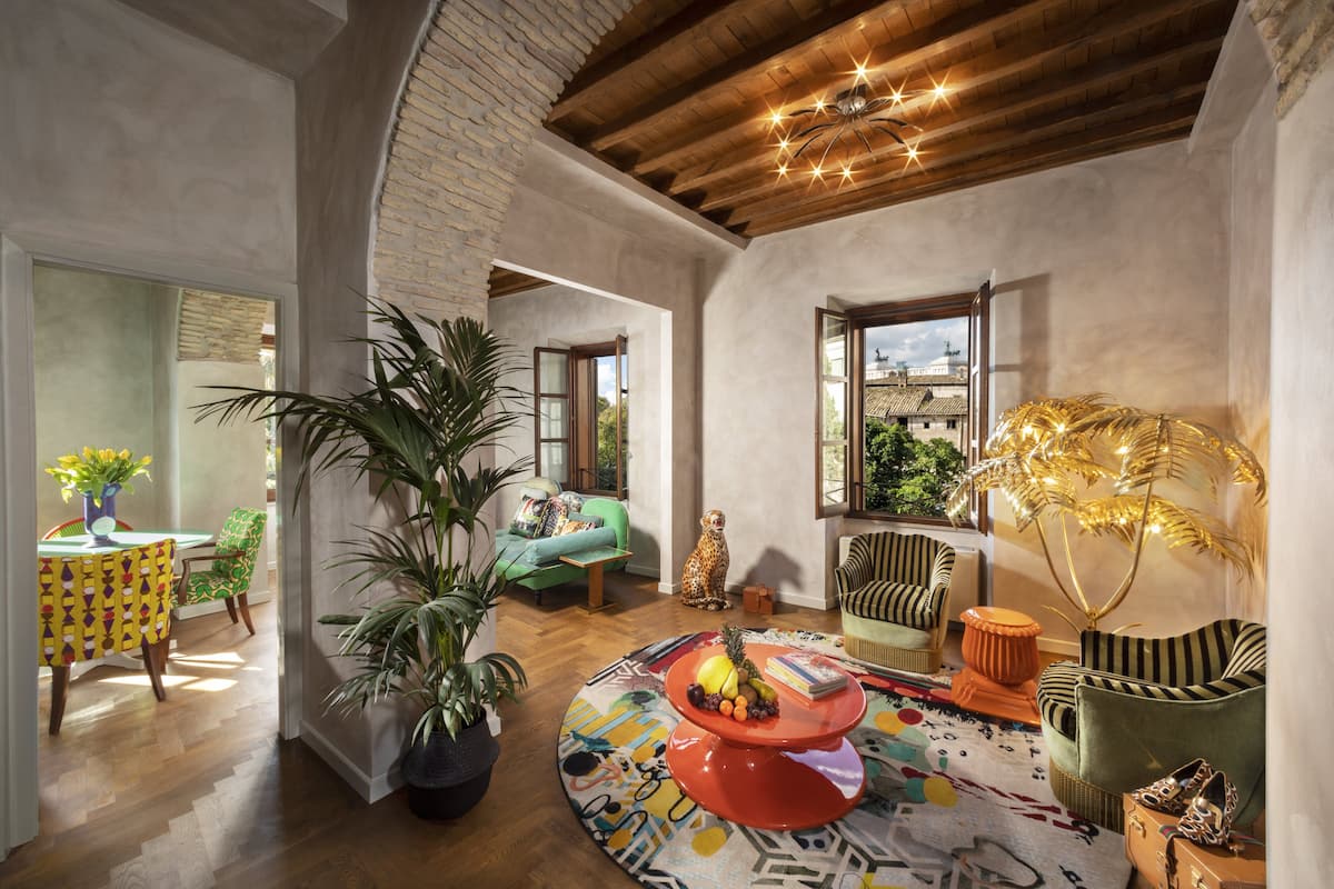 Un salon spacieux avec un plafond en bois, une grande plante en pot, un tapis coloré et une vue sur l’extérieur.