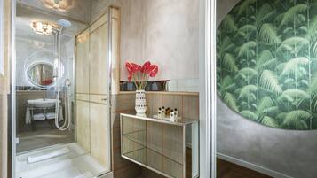 A bathroom with a glass shower enclosure, a sink, a vanity with a mirror, and a decorative wall with a palm tree pattern.