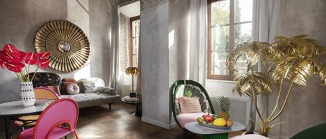 A modern living room with a round table, a pink chair, a green chair, and a large decorative wall piece.
