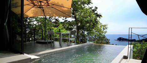 A private infinity pool with a view of the sea, a table and chairs under a canopy, and lush greenery.
