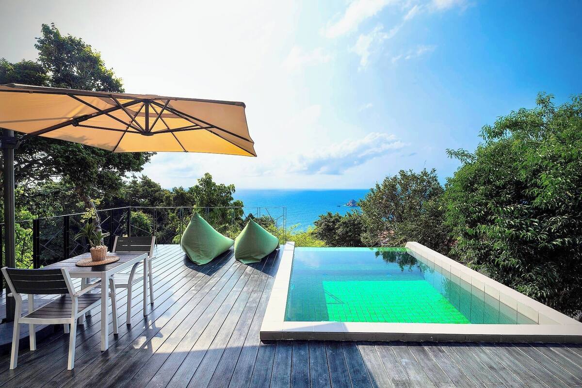 Eine Holzterrasse mit Pool, Sitzgelegenheit und Meerblick.