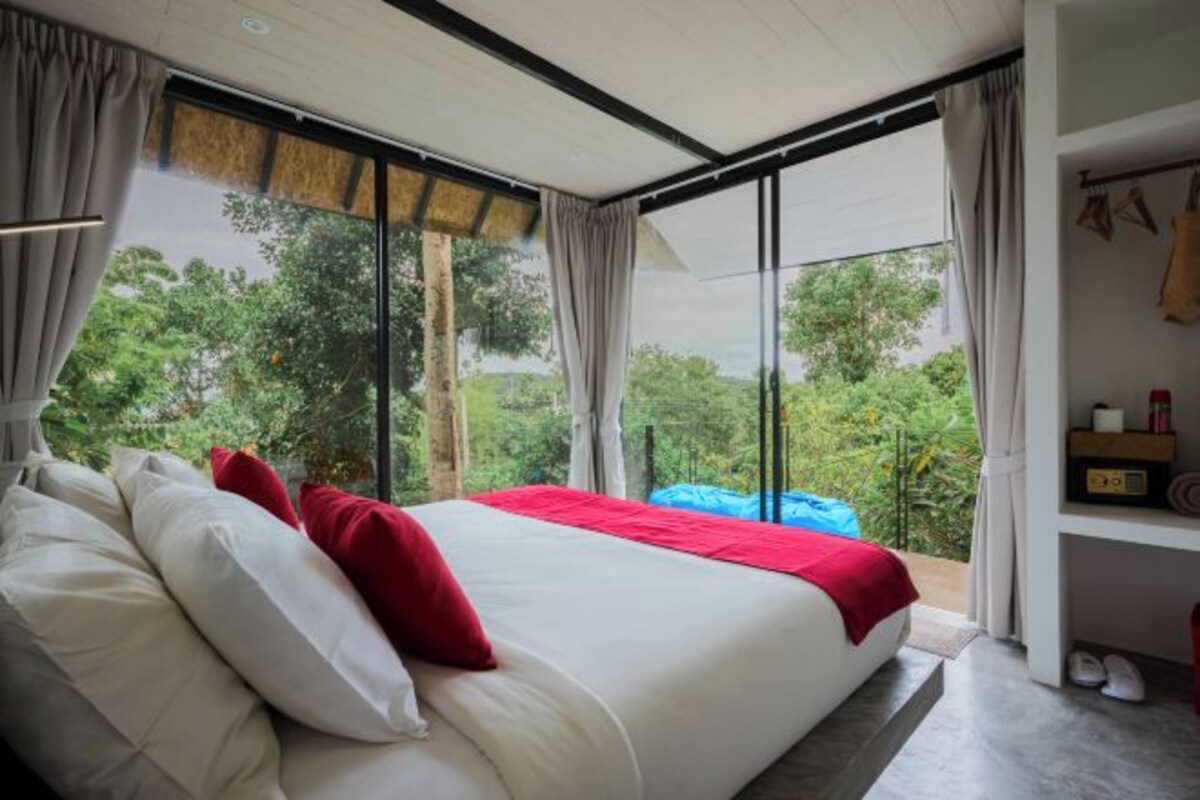 Un dormitorio moderno con una cama grande, vista a un espacio verde, y una estantería con objetos personales.