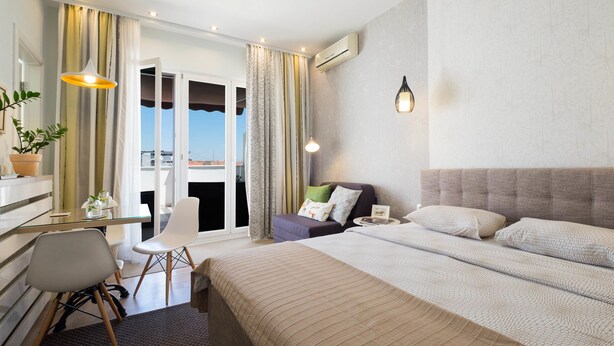 Ein Hotelzimmer mit einem Bett, einem Schreibtisch, einem Sessel und einer Couch, sowie einem Balkon mit Vorhängen.