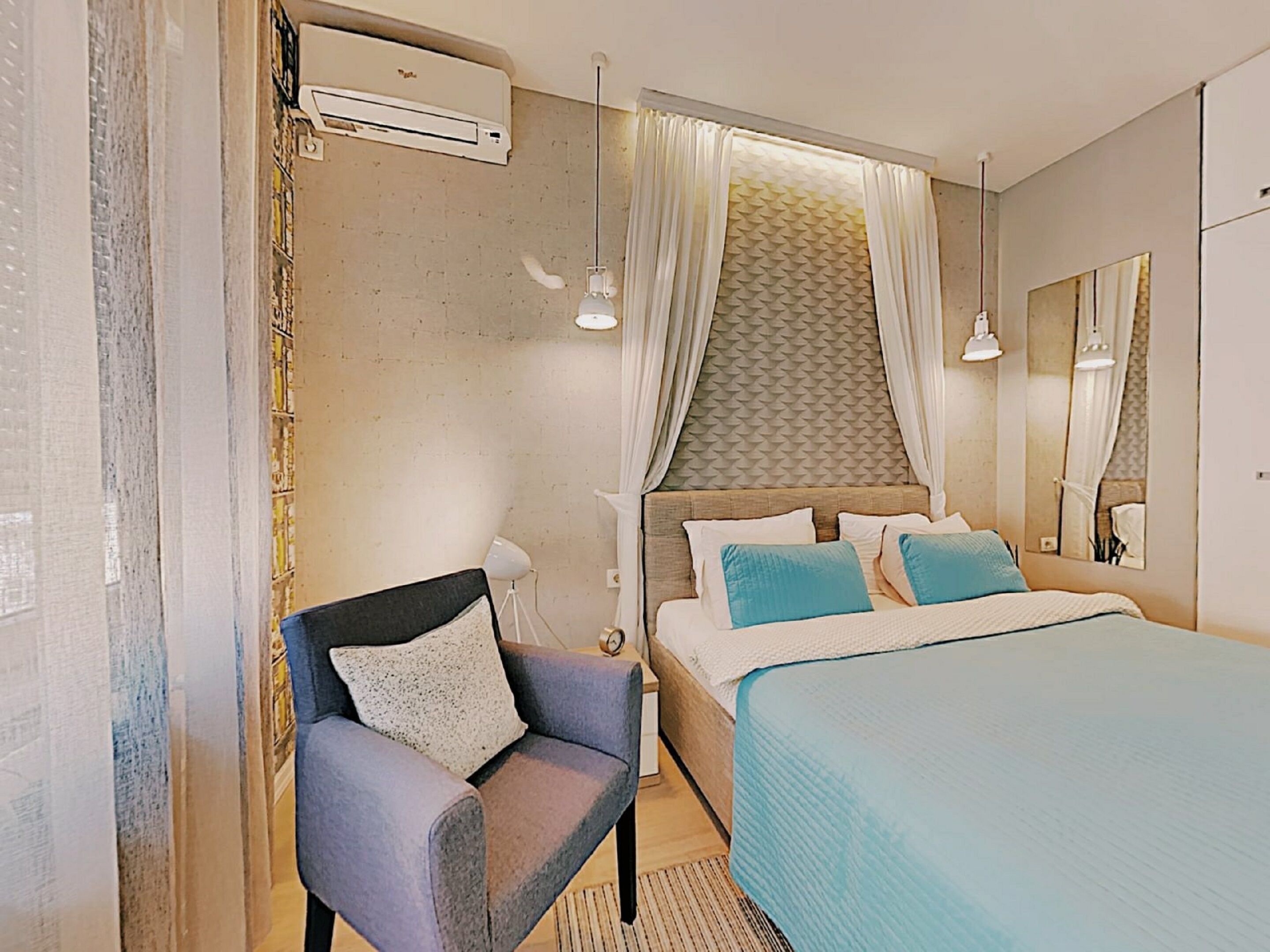 A hotel room with a bed, a chair, a mirror, and an air conditioning unit.