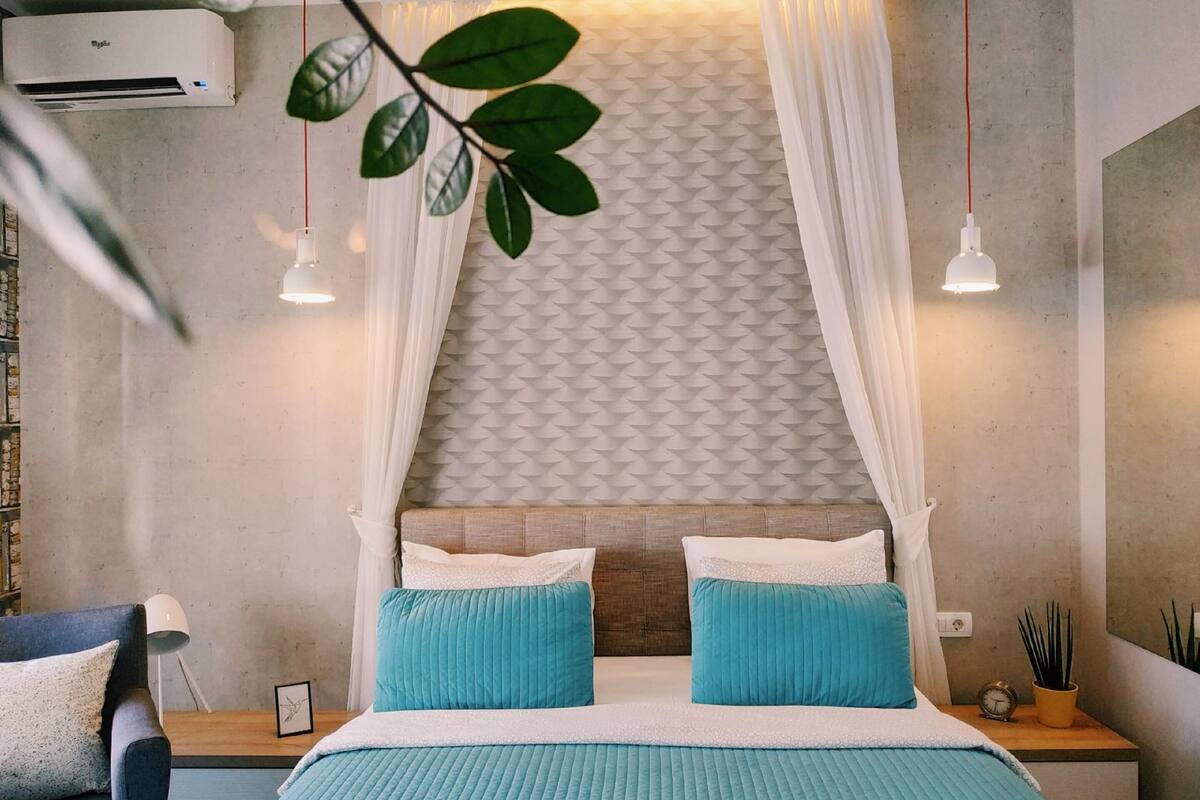 A bedroom with a bed, a nightstand, a lamp, and a wall-mounted air conditioner.