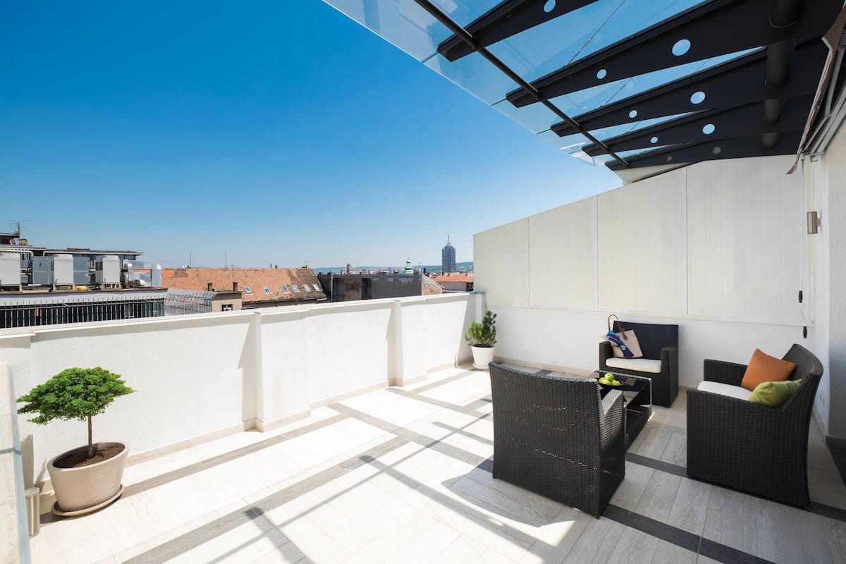 A rooftop terrace with a seating area, potted plants, and a city view.