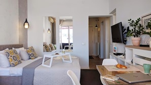 Ein modernes Hotelzimmer mit Bett, Sitzecke mit Tisch und Stühlen, Fernseher und einer Topfpflanze.