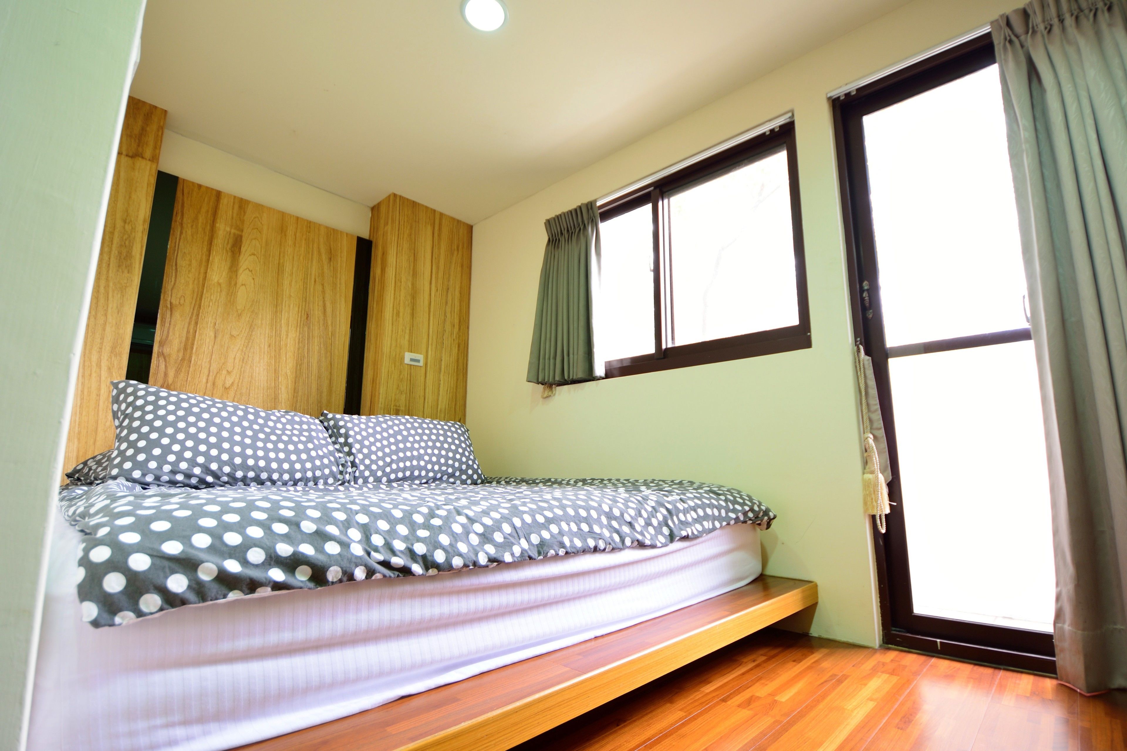 Un dormitorio con cama, suelo de madera, ventana con cortinas y una puerta.