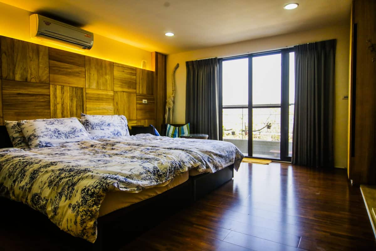 Quarto com cama grande, cabeceira de madeira e porta de vidro deslizante que dá para uma varanda.