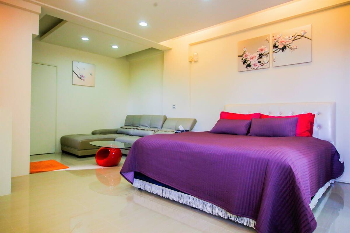 Quarto moderno com uma cama grande, um sofá e uma mesa de centro vermelha.