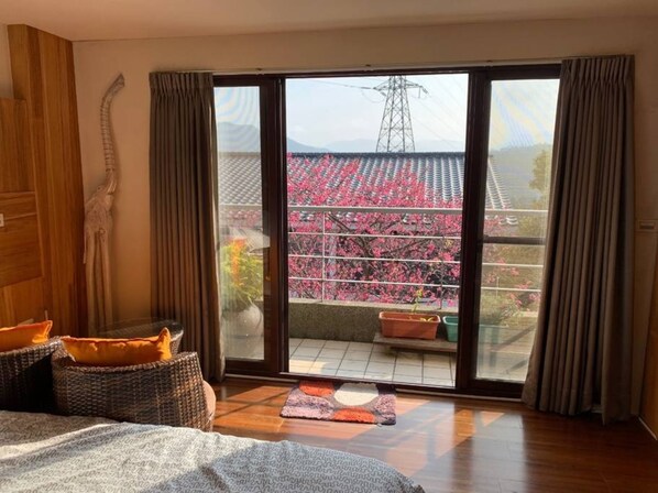 Habitación de hotel con un amplio ventanal corredera que da a un balcón con vistas a flores de cerezo.