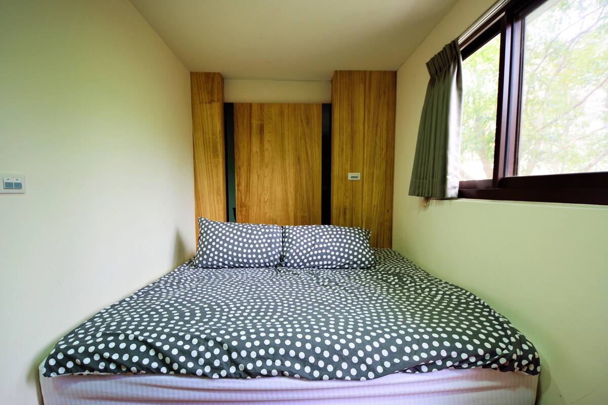 Quarto com cama, paredes de painel de madeira, janela com cortinas e termostato na parede.