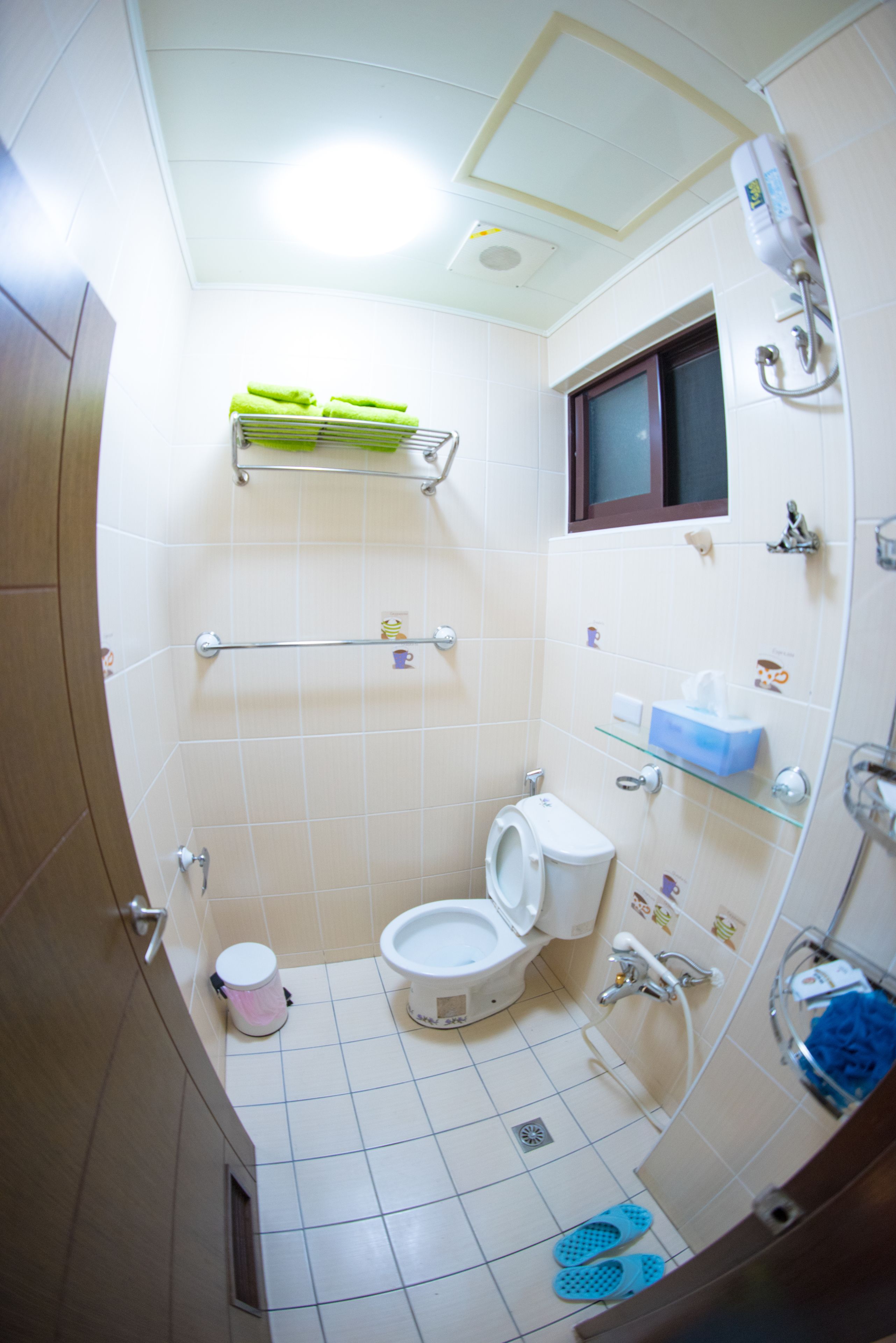 Une petite salle de bain carrelée, équipée de toilettes, d’une étagère avec des articles de toilette et d’un espace douche.