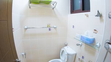 Une petite salle de bain carrelée, équipée de toilettes, d’une étagère avec des articles de toilette et d’un espace douche.