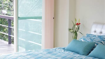 Un dormitorio con un ventanal grande, una cama con ropa de cama azul y un cabecero blanco.