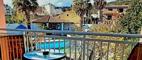 A balcony with a table and chairs, overlooking a swimming pool and a residential area with palm trees and houses.