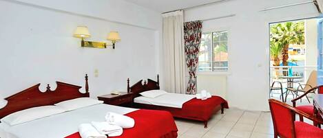 Habitación de hotel con dos camas, ventilador de techo, ventana con cortinas, una mesita con una silla y vista al exterior.