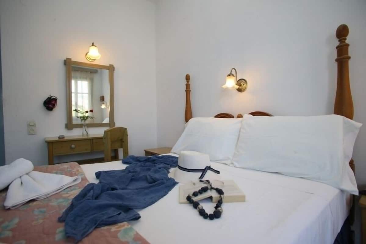 A hotel room with a bed, a bedside table, a mirror, and wall-mounted lights.