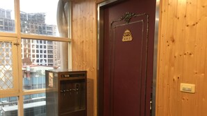 Eine Holztür mit Schild und kleinem Wappen, ein Verkaufsautomat und ein Fenster mit Blick auf Gebäude.
