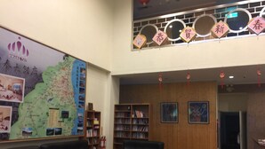 Eine Lobby mit einer großen Karte, zwei schwarzen Sofas mit bunten Kissen, einem Bücherregal und einer Holzwand mit gerahmten Bildern.