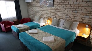 A hotel room with two beds, red chairs, a brick wall, and a painting. - Kilcoy Gardens Motel (Kilcoy)