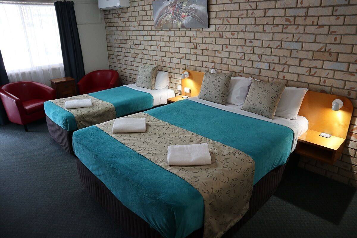 A hotel room with two beds, red chairs, a brick wall, and a painting.