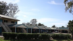 A row of motel buildings with a central staircase, surrounded by well-maintained hedges and trees. - Kilcoy Gardens Motel (Kilcoy)