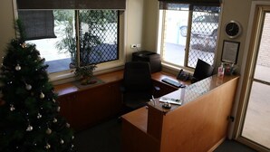 A reception desk with a computer, a clock, and a small plant. - Kilcoy Gardens Motel (Kilcoy)